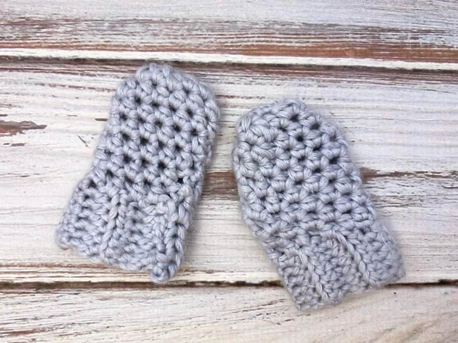 baby crochet mittens lying flat on wooden background